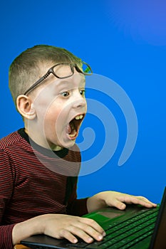 Concept on the theme of children`s curiosity and surprise. A 6-8 year old Caucasian preschool boy sitting in front of a laptop we