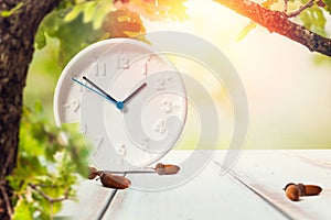 The concept of time change. Clocks and leaves on a wooden white table with acorns. Copy space