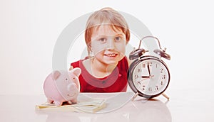 Concept: time is money. Cute little child girl holding a clock and piggy bank
