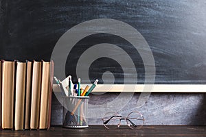 Concept to teacher`s day. Pens, pencils, books and glasses on the table, against the background of chalkboard. Back to school,