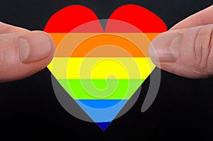 Concept of tolerance towards homosexuals with a gay friendly colored heart exchanged between two men on black background