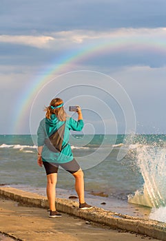 The concept of travel. A hippie blogger girl takes pictures of a rainbow on a mobile phone. Beauty over the sea