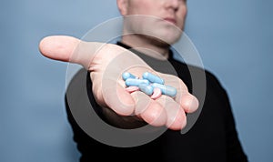 The concept of treatment with antibiotic pills. Medical capsules in a man\'s hand on a blue background.