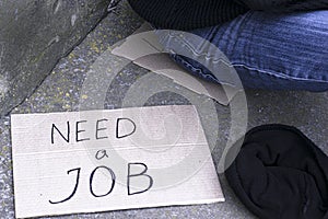 Concept unemployment, poverty, job search, next to an unemployed person sitting on the ground is the hat for alms and a cardboard