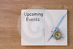 Concept Upcoming Events message on notebook with clock and pencil on wooden table