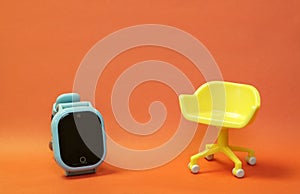 Concept of vacant chair. Yellow stool with blue kid smart watch on orange clean background. Photo in minimal style