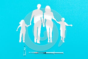 Concept of vaccination and protection against the COVID-19 virus. A silhouette of a family cut out of paper and a syringe with an