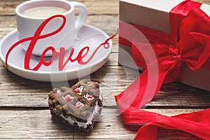 Concept Valentine`s Day. Gift box with red bow and cup of coffee on wooden table. copy space