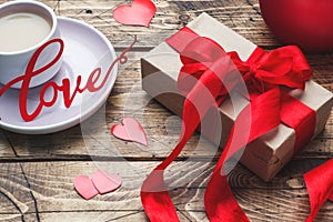 Concept Valentine`s Day. Gift box with red bow and cup of coffee on wooden table. copy space