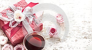 The concept of Valentine`s Day and Mother`s Day, a red gift box with a bow with roses and a cup of tea on a light wooden
