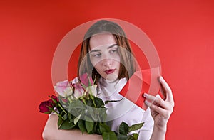 The concept of Valentine& x27;s Day and Women& x27;s Day. Girl holds a bouquet of roses and a note in her hand. A romantic gift.