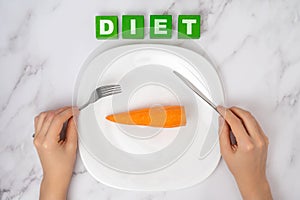 The concept of a vegetable diet. Female hands with a fork and a table knife over an orange carrot lying on a white plate