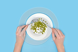 The concept of a vegetable diet and weight loss. Canned green peas in a white plate, a fork and a table knife in women`s hands