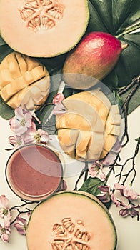 Concept of a vegetarian, healthy food, fresh sliced mango and melon with smoothies, with flowers and leaves of monstera, top view
