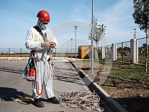 Concept: vertical work. Man with nbc suit, harness, helmet and equipment for height. Preparing rope for climbing
