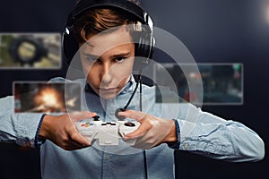 The concept of video games. A teenage boy, in headphones with a serious look playing a game. In the hands of holds joystick. Dark