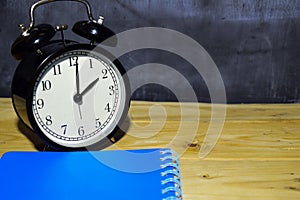 Concept vintage background black retro alarm clock on 14.00 pm or 02.00 am and blue book