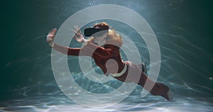 Concept of virtual reality. Beautiful young happy red haired woman using VR headset floating under water slow motion.