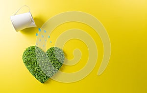 Concept of watering hearts made from grass on yellow background. World environment day, earth day, save earth and eco concept