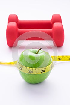 Concept of weight loss with fresh green apple, measuring tape and dumbbells. Fitness diet programme. Top view angle with copy
