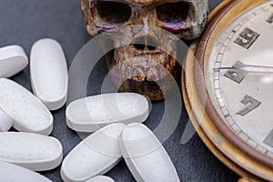 Concept for whom the bell tolls: antique pocket watch, carved skull and medical pills on natural stone