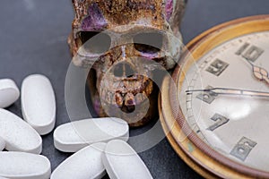 Concept for whom the bell tolls: antique pocket watch, carved skull and medical pills on natural stone