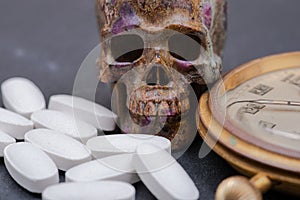 Concept for whom the bell tolls: antique pocket watch, carved skull and medical pills on natural stone