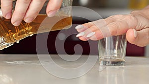 Concept woman denies alcohol and liquor. A woman`s hand gestures forbidding pouring whiskey into a glass from a bottle. A woman wh