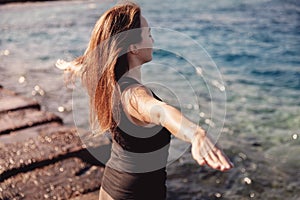 Concept woman power energy healthy life. Girl practices yoga on background of sea, wind blows hair