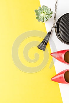 Concept of womanâ€™s outfit with red high heels and purse on yellow background with copyspace. Fashion background.