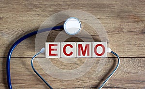 Concept word `ECMO, Extra Corporeal Membrane Oxygenation` on cubes on a beautiful wooden background. Stethoscope. Copy space,