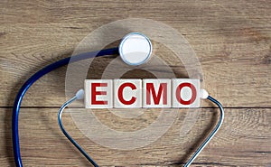 Concept word `ECMO, Extra Corporeal Membrane Oxygenation` on cubes on a beautiful wooden background. Stethoscope. Copy space, photo