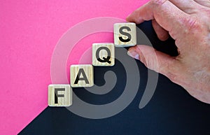 Concept word `FAQS` on cubes on a beautiful black and purple background. Male hand. Business concept