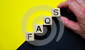 Concept word `FAQS` on cubes on a beautiful blue and yellow background. Male hand. Business concept