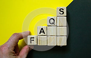 Concept word `FAQS` on cubes on a beautiful blue and yellow background. Male hand. Business concept