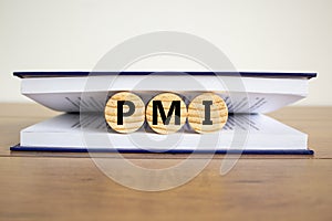 Concept word `PMI - purchasing manager index, ` on wooden circles between pages of a book on a beautiful wooden table. White