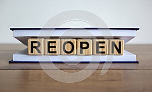 Concept word `reopen` on wooden cubes between pages of a book on a beautiful wooden table. White background. Business concept