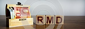 Concept word `RMD` on cubes on a beautiful wooden table, small chest with euro bills. Beautiful background