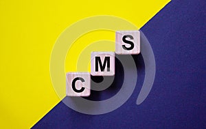Concept words `CMS, content management system` on wooden cubes on a beautiful yellow and black background. Copy space, business