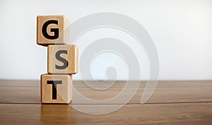 Concept words `GST, goods and services tax` on cubes on a beautiful wooden table, white background. Business concept. Copy space