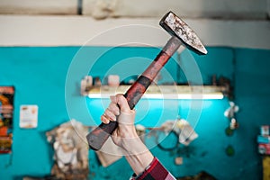 Concept of workplace improvement and worker protest. A woman`s hand is holding a dirty old hammer. Hand close-up. The workshop in