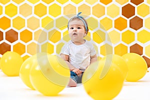 The concept of the World Children`s Day. A cute toddler girl is sitting on a floor with yellow balloons. In the background is