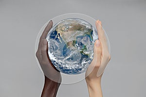 The concept of the world is in your hands. Two white-and black-skinned hands hold the globe against an isolated gray background.