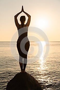 The concept of yoga and sports. Silhouette of a woman standing on a stone, against the sea and sunset. Meditation and yoga classes