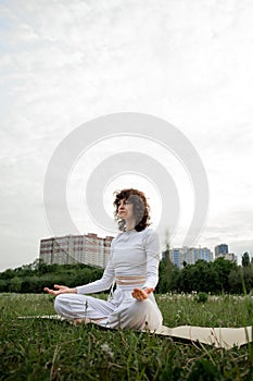 Concept of yoga training on fresh air. Young girl meditating in lotus pose. Female coach practicing retreat outdoor