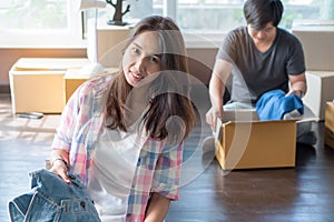 Concept young couple moving house. Asian young couple unpack cardboard box after moving in new house