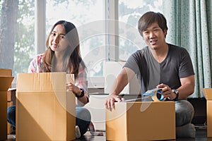 Concept young couple moving house. Asian young couple unpack cardboard box after moving in new house