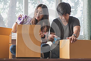 Concept young couple moving house. Asian young couple unpack cardboard box after moving in new house