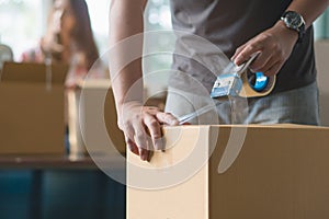 Concept young couple moving house. Close-up hand of man use tape sealing cardboard box