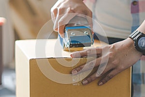 Concept young couple moving house. Close-up hand of woman use tape sealing cardboard box